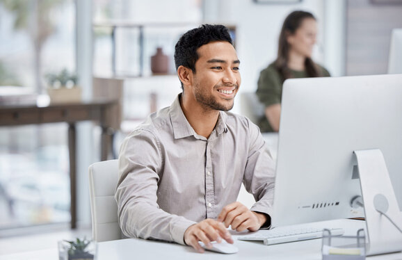 young man with grey shirt smiling while using desktop pc - devicenow. True subscription worldwide